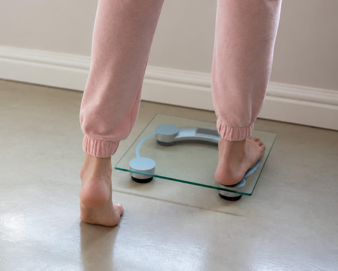 Kvinne i rosa joggebukse går opp på en badevekt