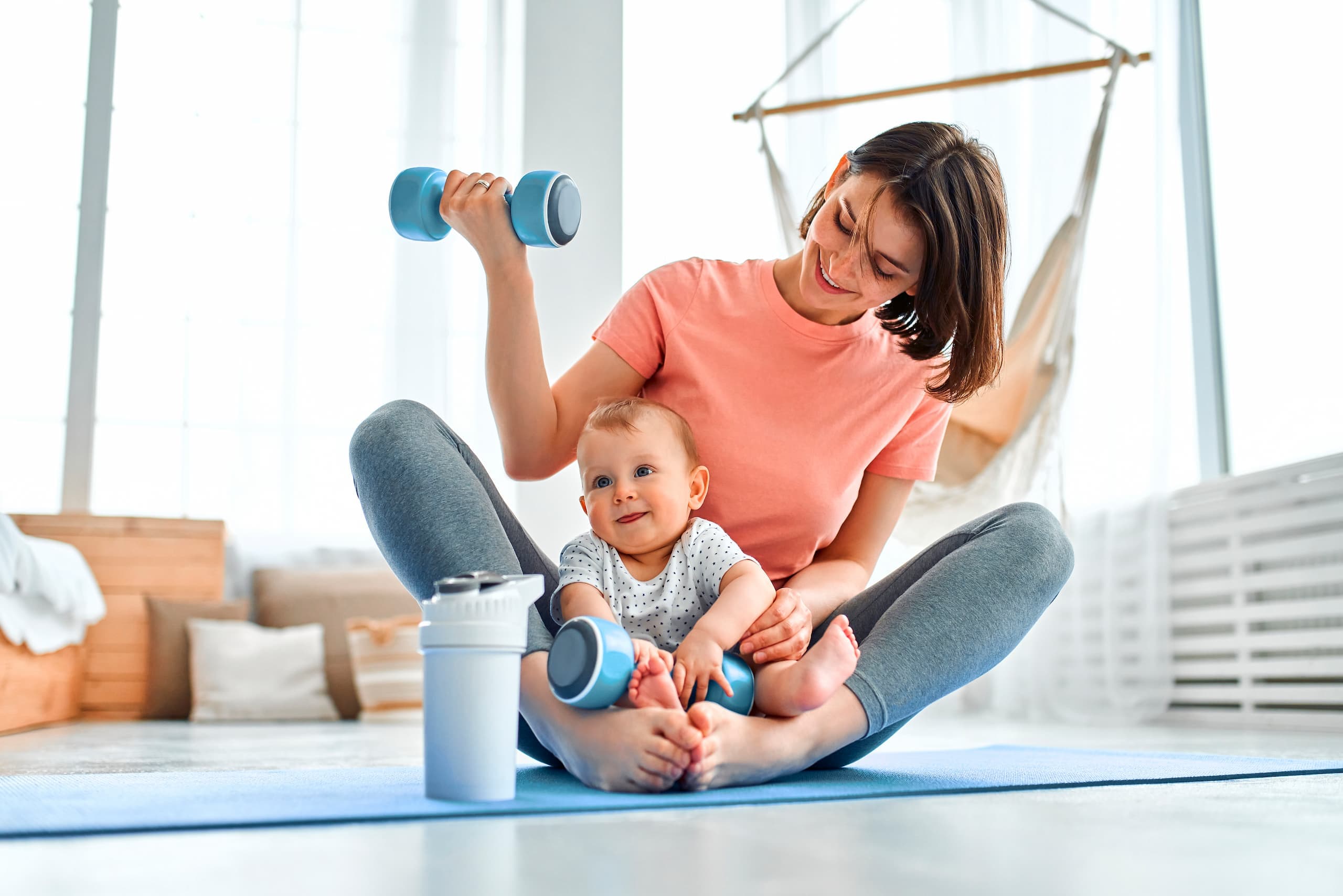 Mor trener med manualer på en yogamatte med babyen i fanget